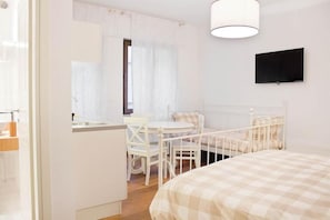Un dormitorio con una cama, una mesita de noche, una silla, una pequeña mesa y un televisor fijado a la pared.