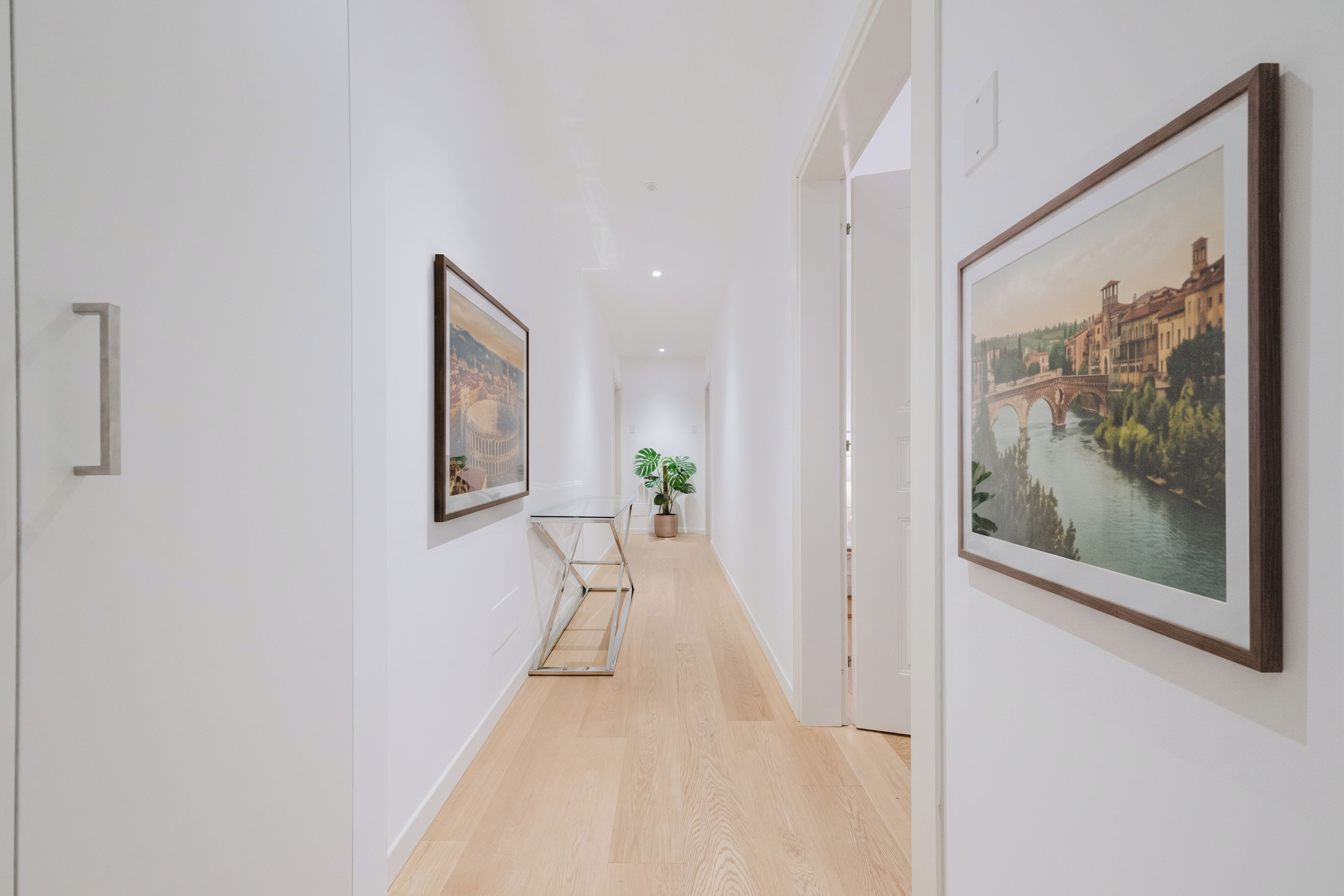 A hallway with framed artwork on the walls, a potted plant, and a wooden floor.