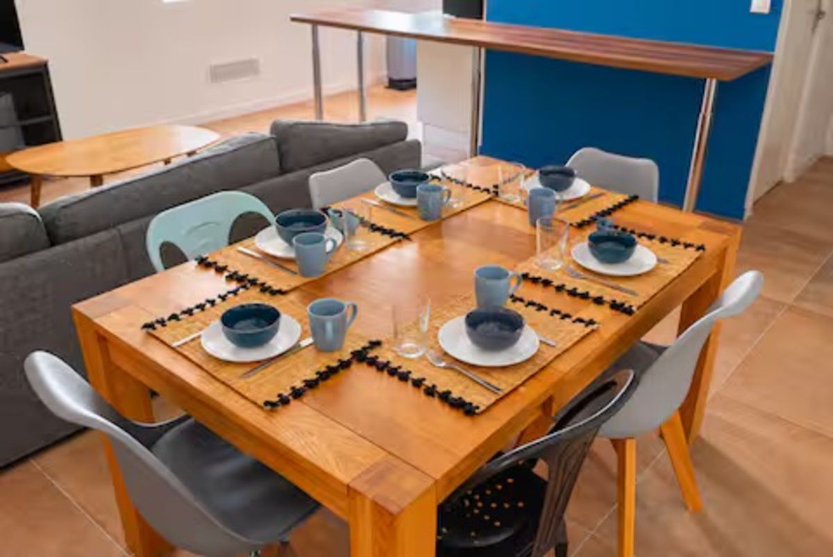 Un coin repas avec une table en bois dressée pour six personnes, entourée de chaises grises.