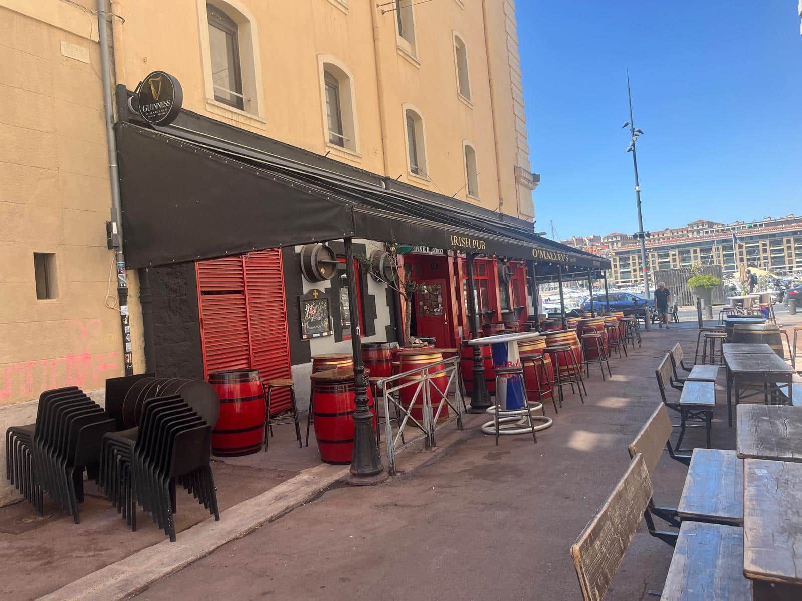 Area esterna con tavoli e sedie, una botte rossa e un cartello per un pub irlandese.