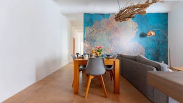 Un comedor con una mesa dispuesta para dos personas, un sofá y un cuadro abstracto grande en la pared.