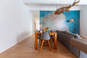 Zona pranzo con tavolo apparecchiato per due, divano e un grande quadro astratto appeso al muro.