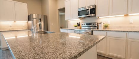 A modern kitchen with granite countertops, stainless steel appliances, and white cabinetry.