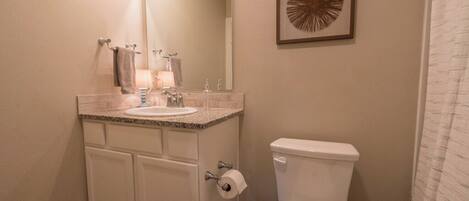 A bathroom with a sink, mirror, toilet, and a framed artwork on the wall.