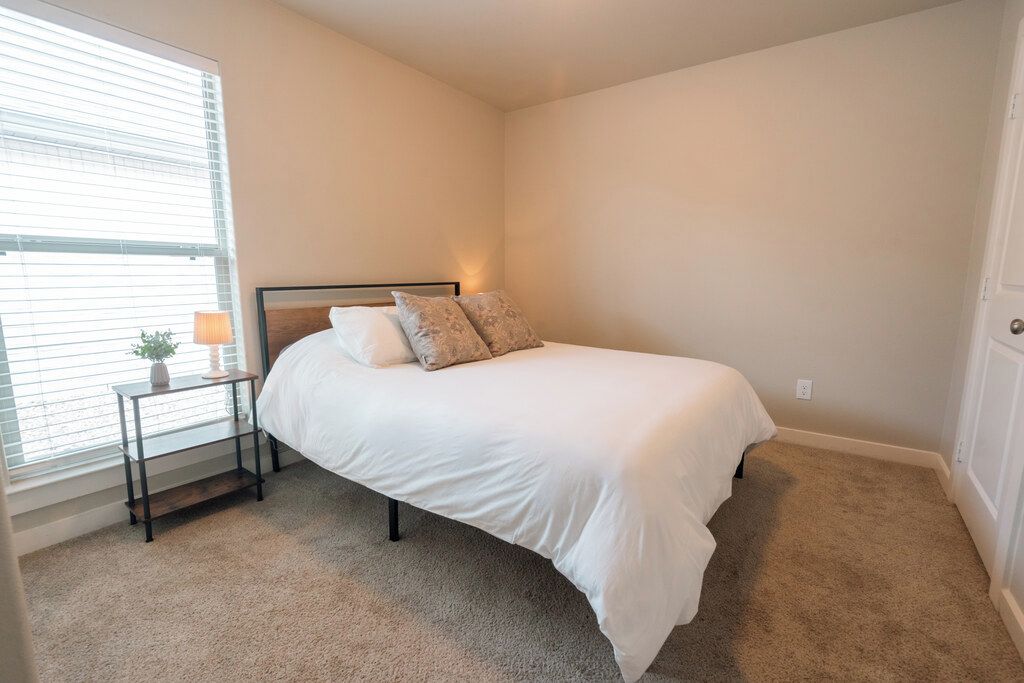 A bedroom with a single bed, a bedside table with a lamp, and a window with blinds.
