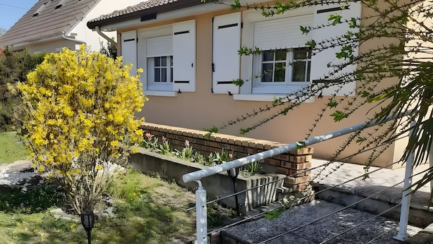En boligbygning med en trappe, der fører til en lukket indgang, omgivet af en have med et blomstrende, gult træ.