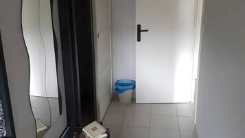 Un couloir avec une porte blanche, une poubelle bleue et un miroir accroché au mur.