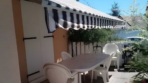 En terrasse med bord og stole, et overdækket siddeområde og en potteplante.