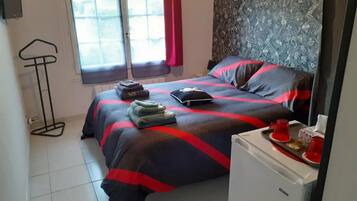 A bedroom with a bed, a small fridge, a window with curtains, and a wall with a floral pattern.
