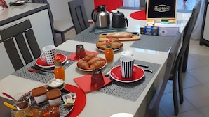 Et spiseområde med et bord dækket til morgenmad, inklusive brød, kager, tilbehør og en kaffemaskine.