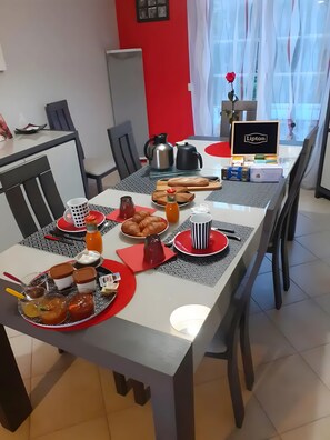Ruokailutila, jossa on aamiaiselle katettu pöytä: pöydällä on leipää, leivonnaisia, lisukkeita ja kahvinkeitin.