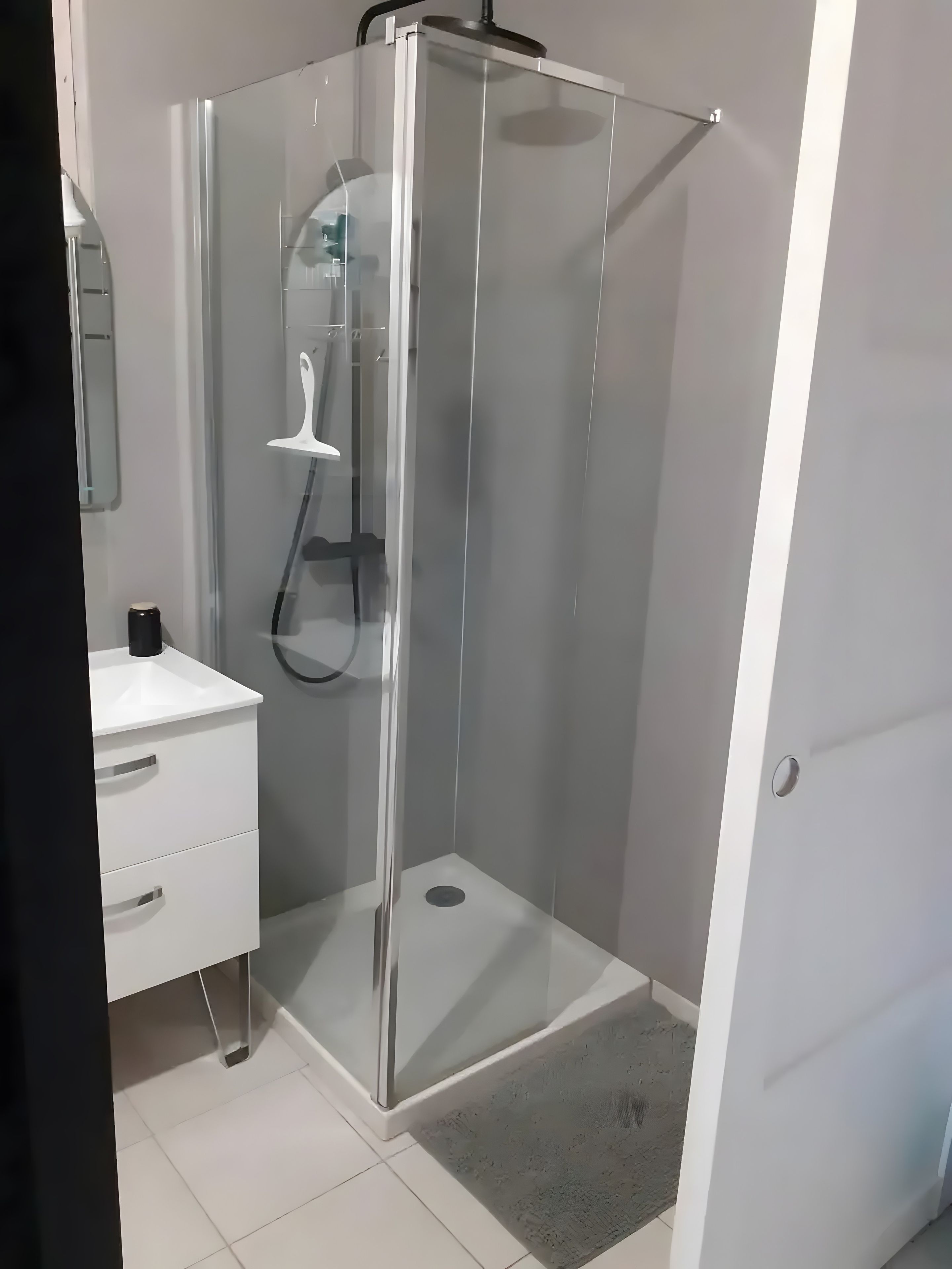 Une salle de bain avec une douche à parois de verre, un lavabo blanc avec un miroir et un meuble blanc.