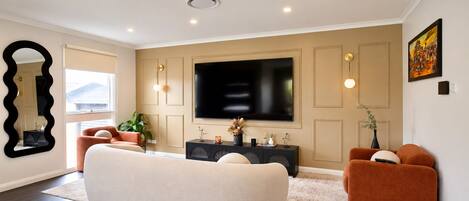 A modern living room with a large flat-screen TV, a sofa, a coffee table, and a side table with decorative items.
