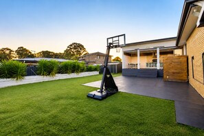 A residential backyard with a lawn, a basketball hoop, and a covered patio area. - Stylish Family Retreat with Sauna, Gym, Basketball & Alfresco (Saint Clair)