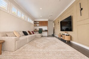 A living room with a sectional sofa, a flat-screen TV, and a patterned rug. - Stylish Family Retreat with Sauna, Gym, Basketball & Alfresco (Saint Clair)