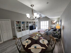 A dining area with a round table set for four, a built-in entertainment unit, and a sofa in the background. - Premium Peaceful Intracoastal Retreat | 2BR • 2BA • Sleeps 6 (Indian Shores)