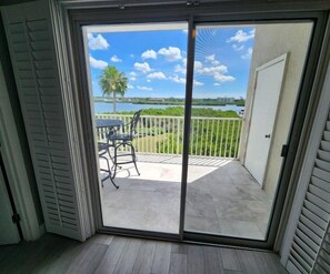 A room with a sliding glass door leading to a balcony with a view of a body of water and palm trees. - Premium Peaceful Intracoastal Retreat | 2BR • 2BA • Sleeps 6 (Indian Shores)