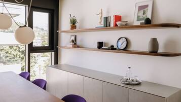 Un comedor moderno con una mesa de madera, sillas moradas y un armario gris. Hay dos estantes sobre el armario con libros, un reloj y objetos decorativos.