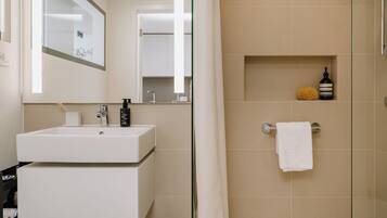 Un baño moderno con lavamanos, espejo y zona de ducha blancos.
