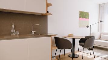 Una cocina moderna con un lavaplatos integrado, una zona de comedor con dos sillas y un sofá blanco al fondo.