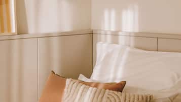 Un lit avec une literie blanche et deux oreillers, dont l’un présente un motif texturé et l’autre est uni.