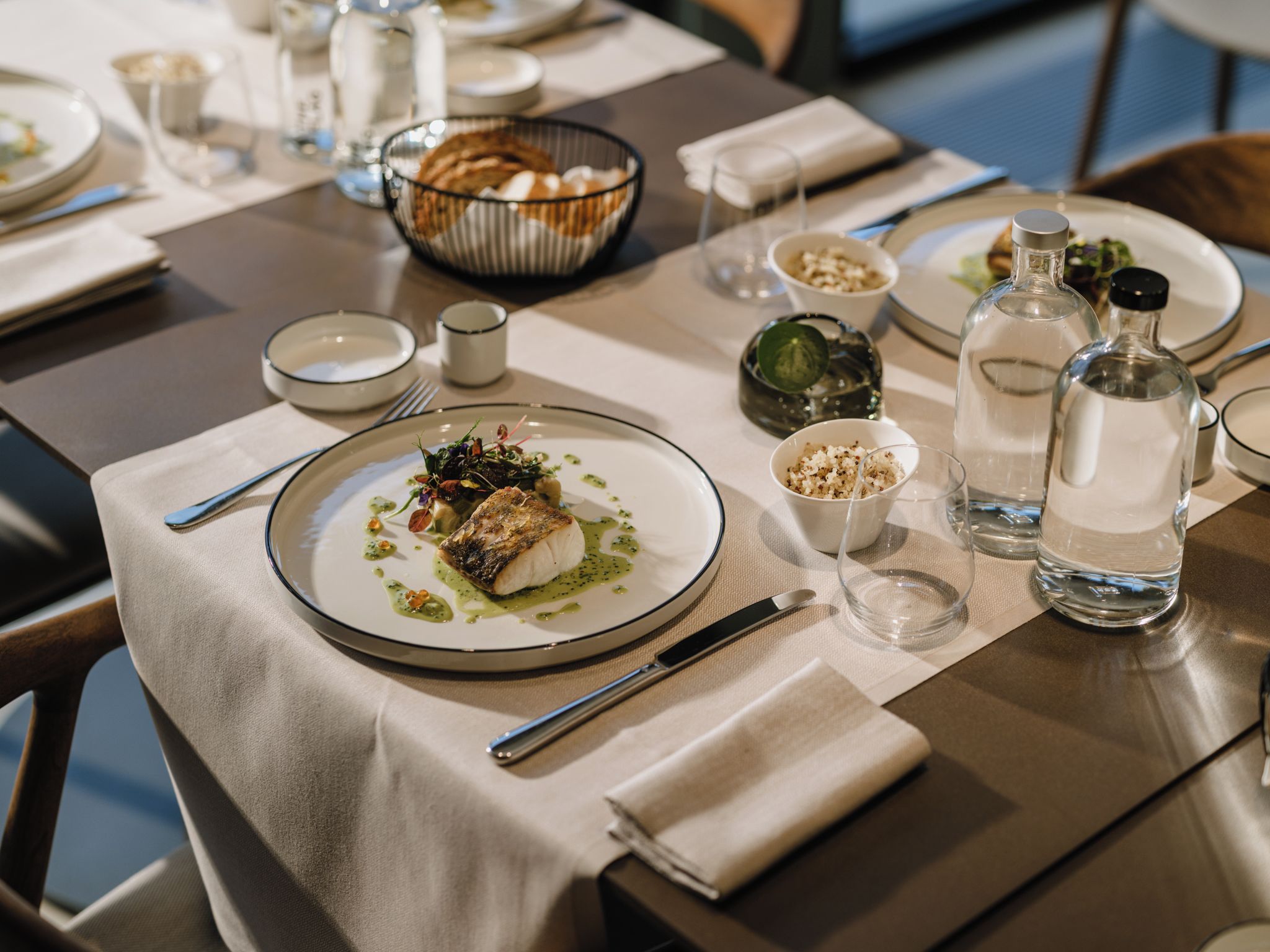 Una mesa de comedor dispuesta con platos, cubiertos y una botella de agua.