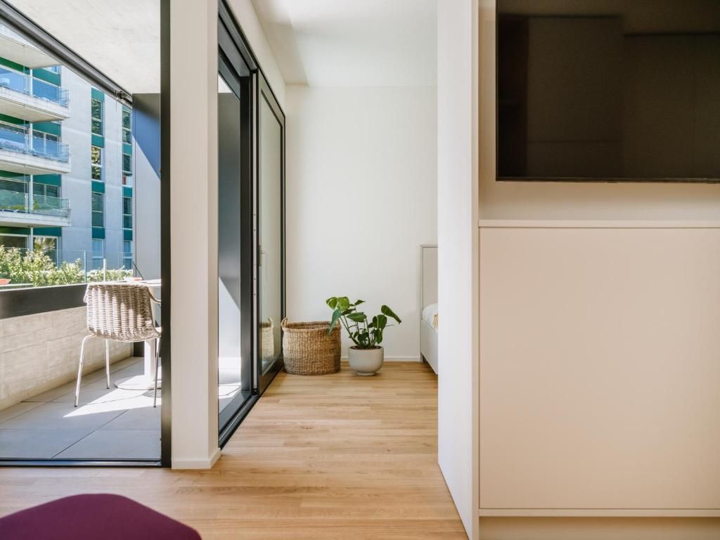 Un interno moderno con parquet, una grande finestra, una sedia in vimini e una pianta in vaso.