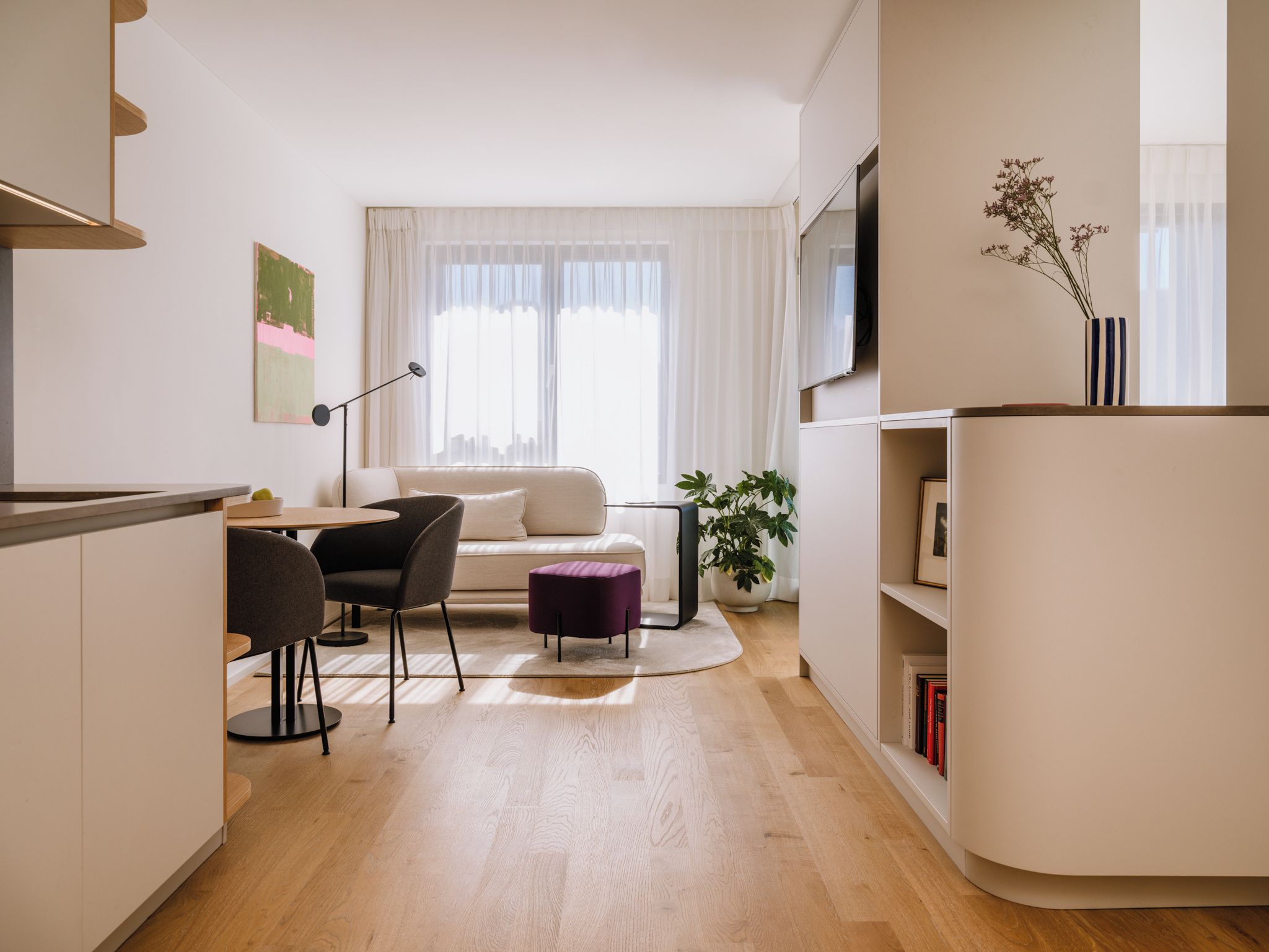 Un salon moderne comprenant un canapé, une table à manger avec des chaises, un petit pouf violet, une plante en pot et une bibliothèque.