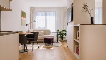 Un salon moderne comprenant un canapé, une table à manger avec des chaises, un petit pouf violet, une plante en pot et une bibliothèque.