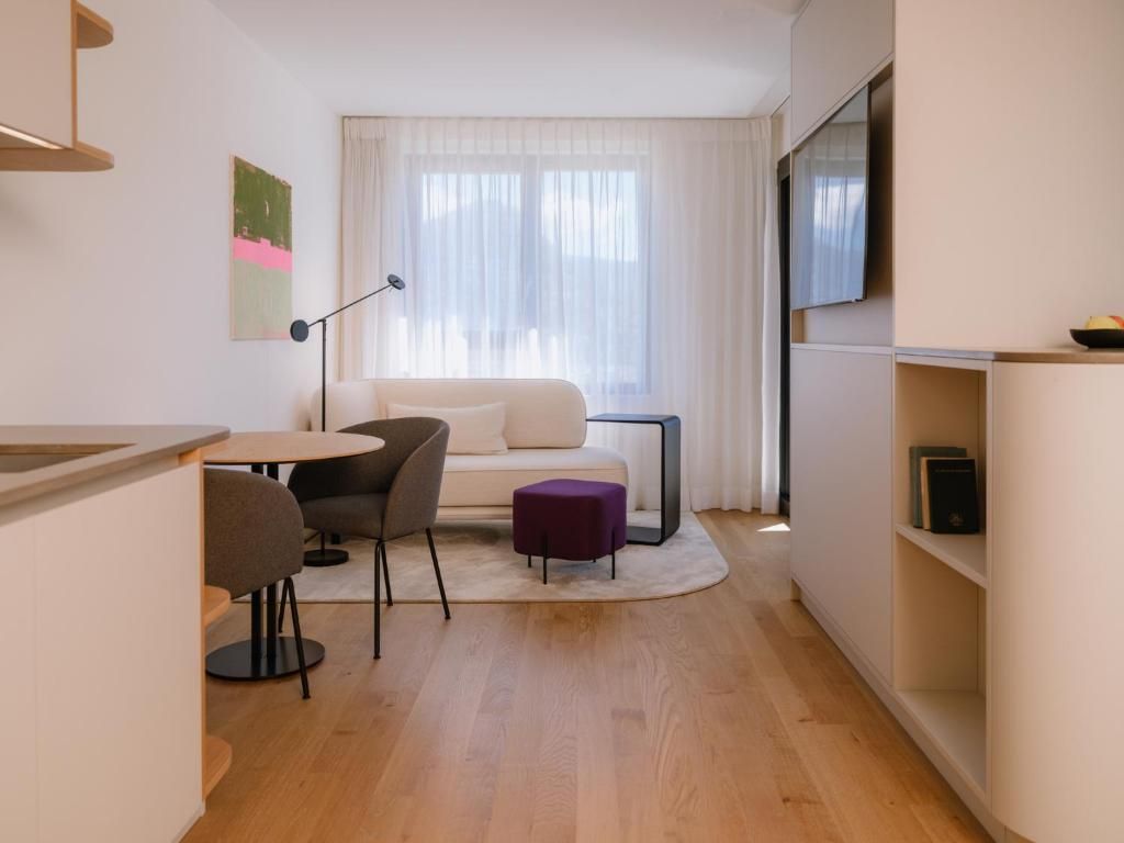 Un salon moderne comprenant un canapé, des fauteuils, une petite table, un téléviseur et une bibliothèque.