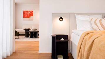 A modern bedroom with a bed, bedside tables, a nightstand, a wall-mounted light, and a painting on the wall.