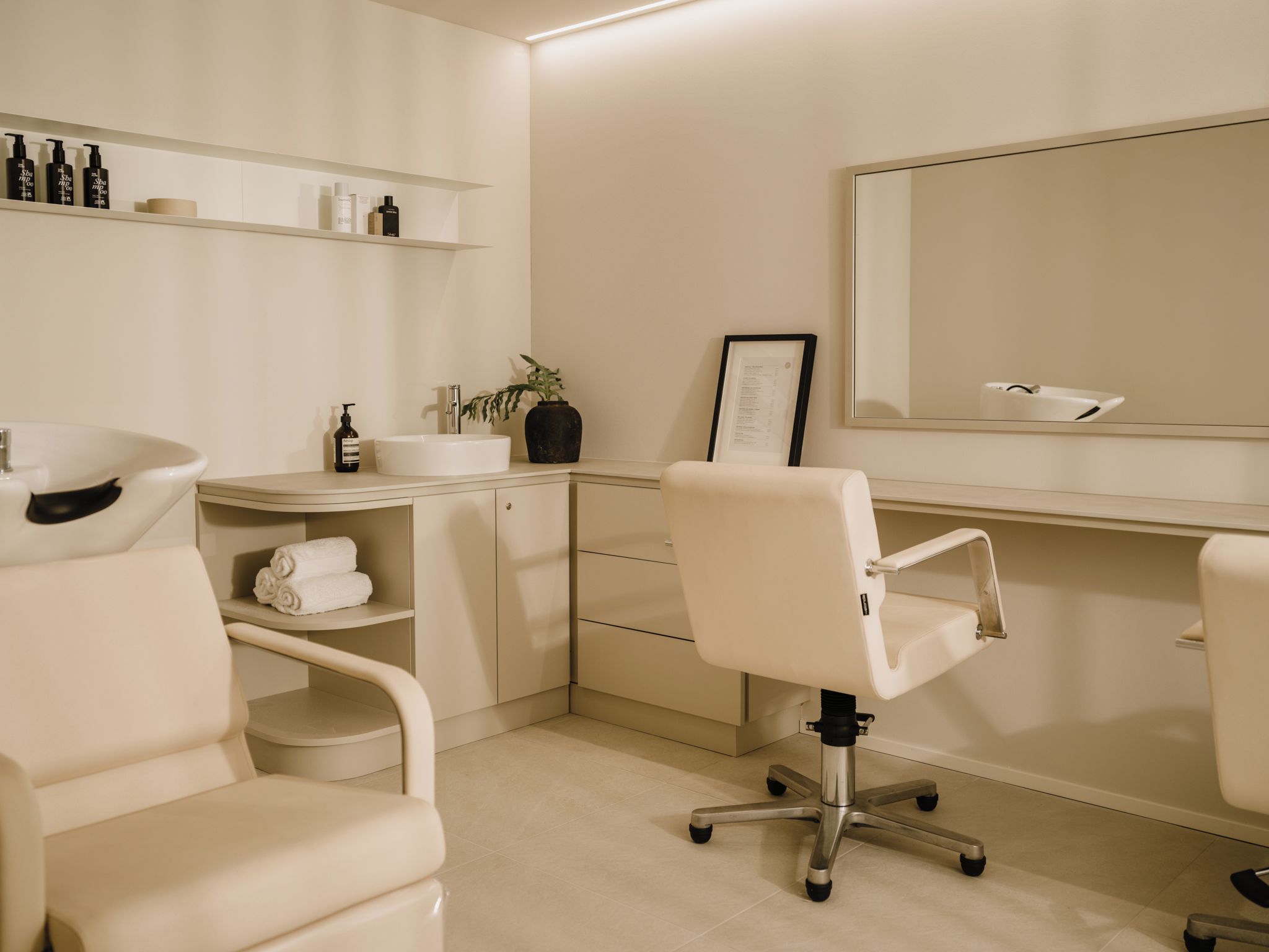 Une salle de bain moderne avec un lavabo blanc, un miroir, une chaise et des étagères contenant des articles de toilette.