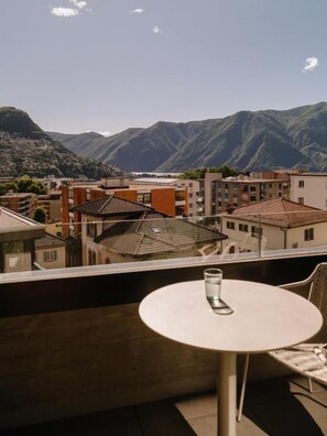 Ein Balkon mit Tisch und Stühlen, der auf eine Stadt mit Gebäuden und Bergen im Hintergrund blickt.