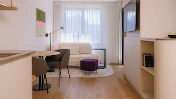 Uma sala de estar moderna com um sofá, duas poltronas, uma mesinha, um banquinho roxo, um abajur e uma TV de tela plana fixada na parede.