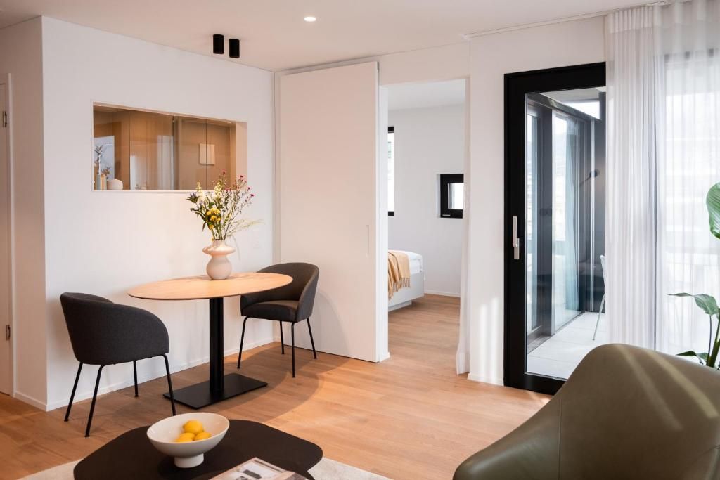 Habitación de hotel moderna con zona de comedor, cama y vistas a través de un ventanal.
