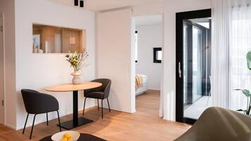 Habitación de hotel moderna con zona de comedor, cama y vistas a través de un ventanal.