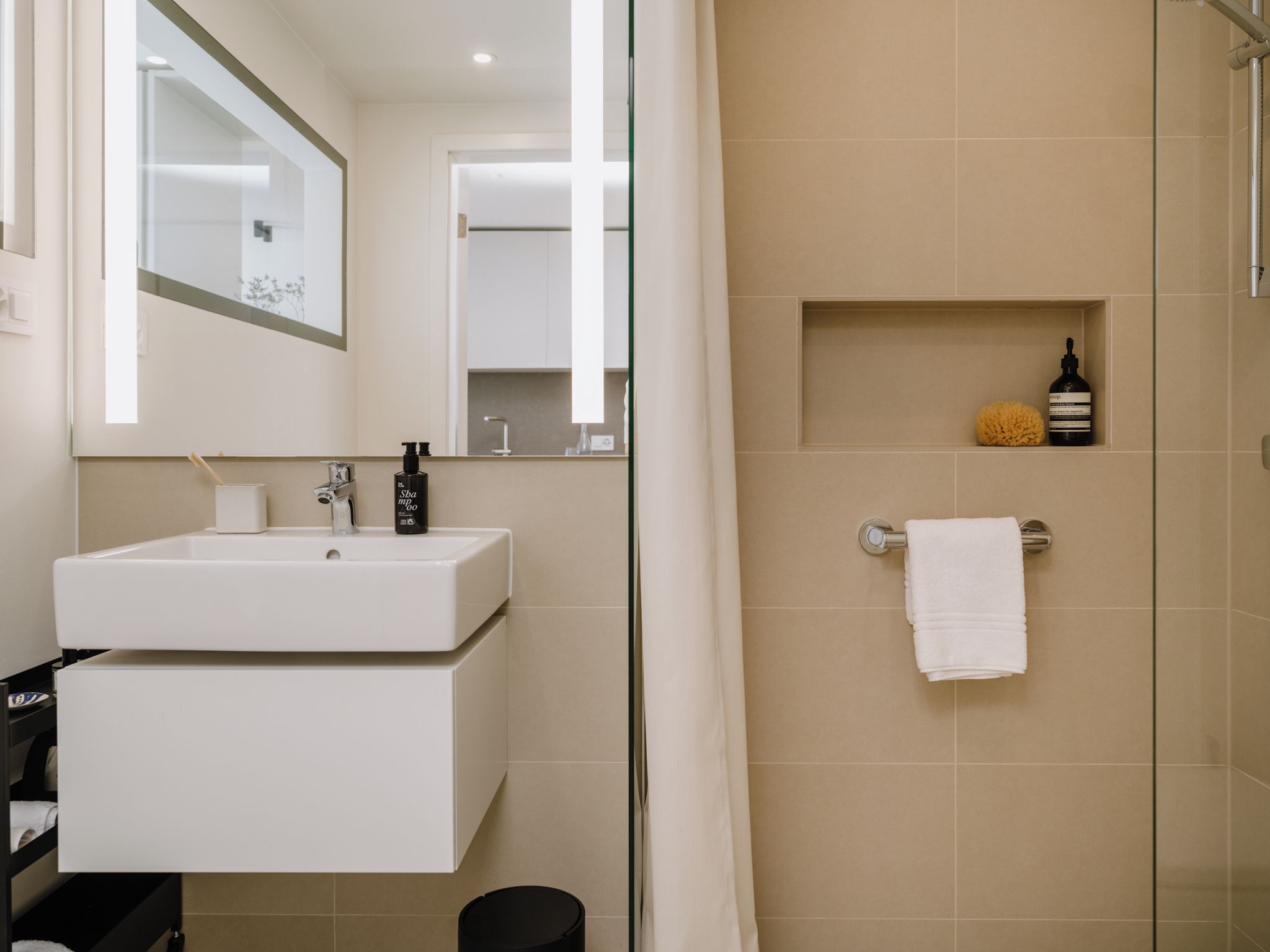 A modern bathroom with a white sink, mirror, and shower area.