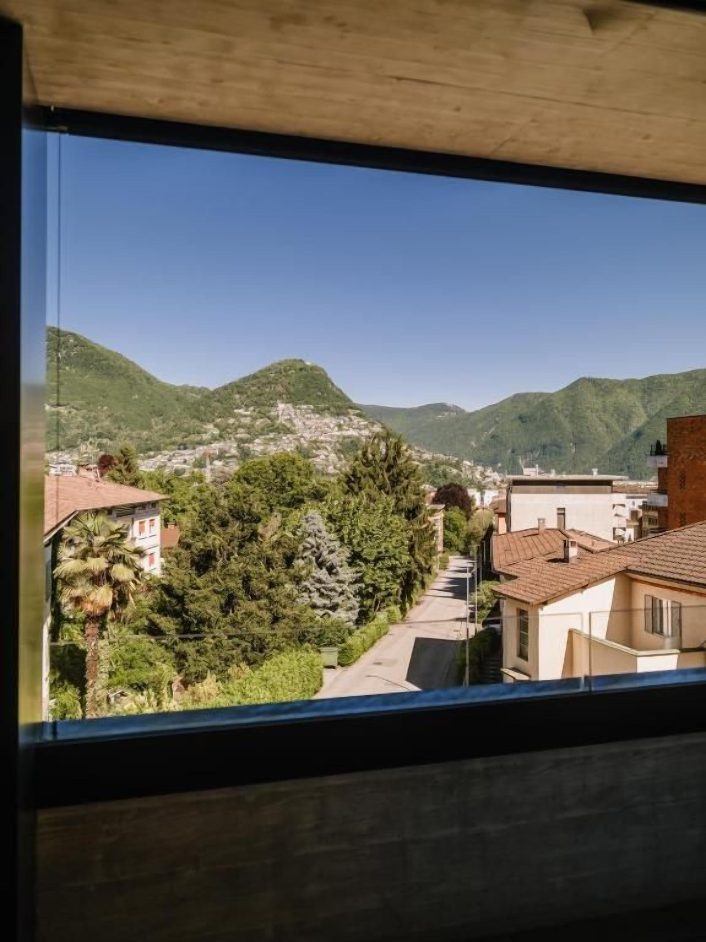 Une vue depuis une fenêtre donnant sur une colline, avec des bâtiments et de la végétation.