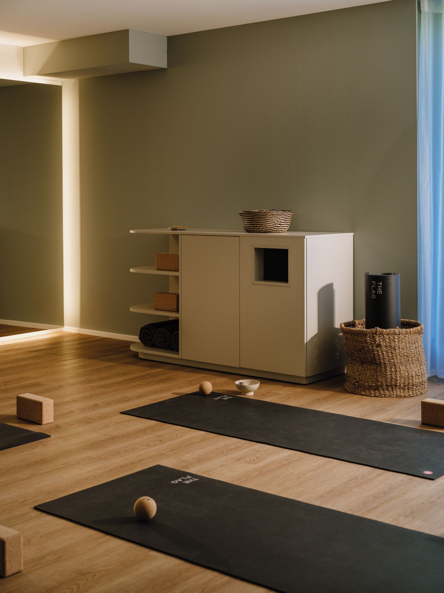 A room with a wooden floor, a cabinet with shelves, a yoga mat, and a basket.