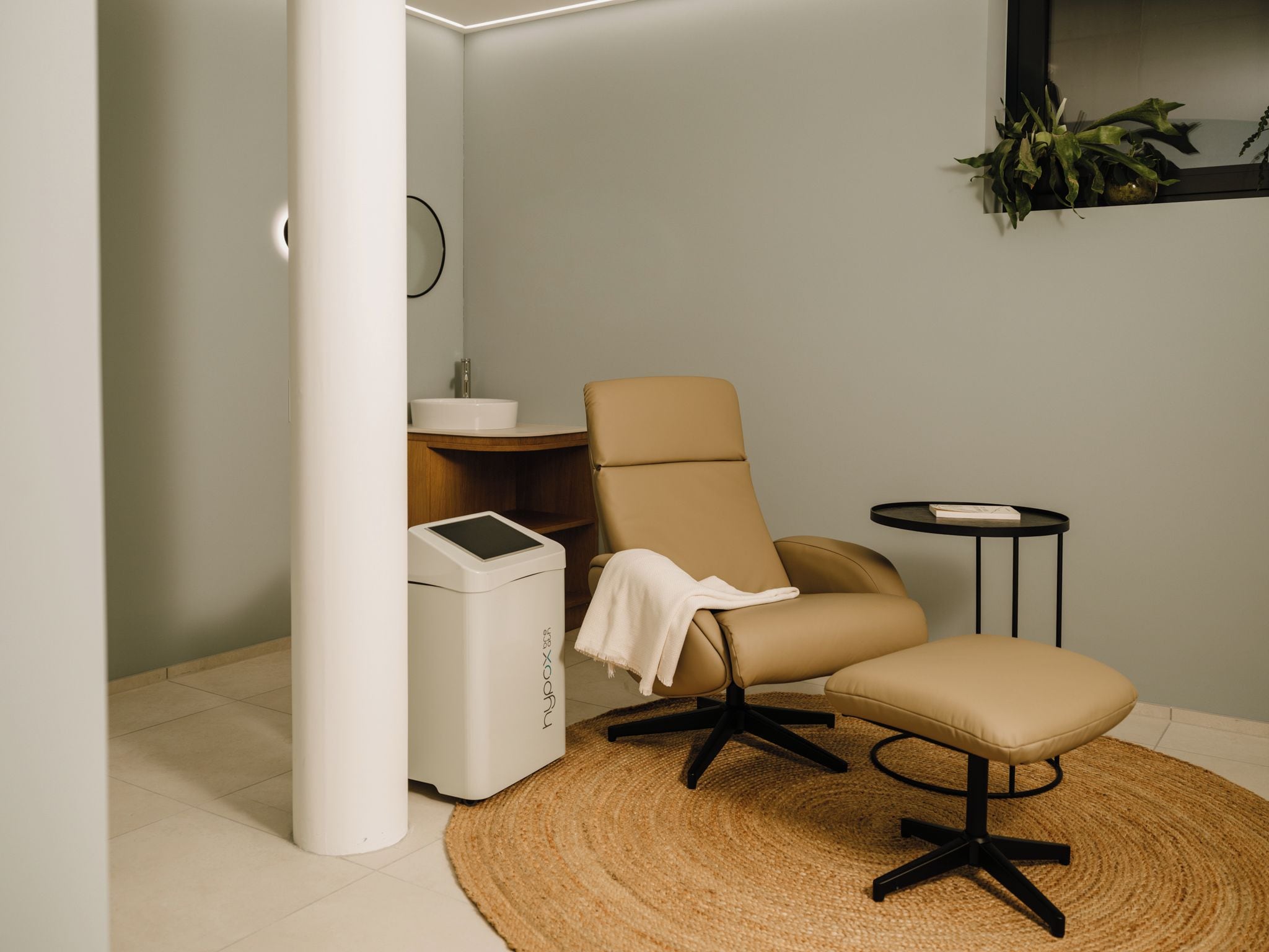 A modern bathroom with a beige chair, a small round table, and a white washing machine.