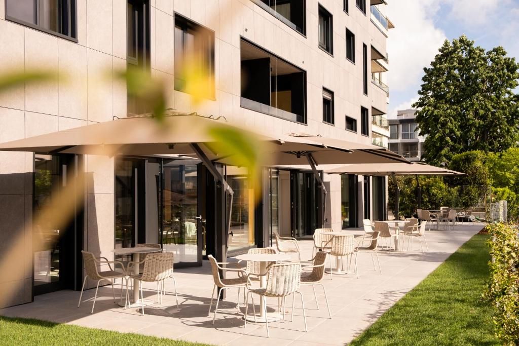 An outdoor seating area with tables and chairs, a covered patio, and a building with large windows and balconies.