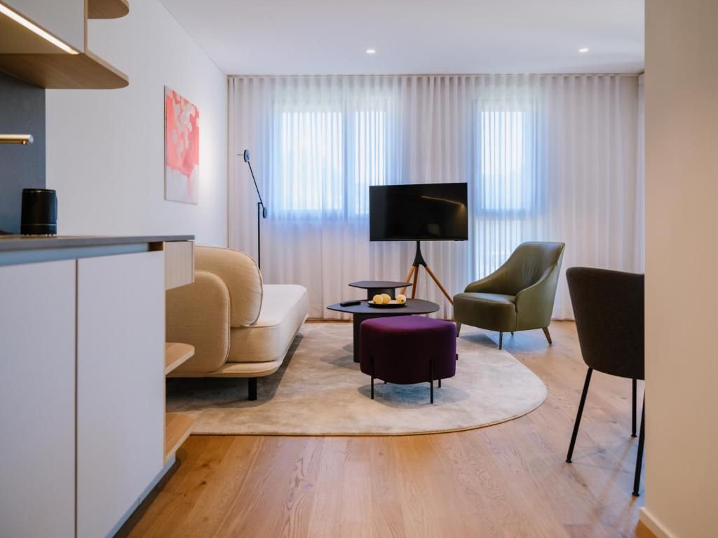 Un salon moderne comprenant un canapé, un fauteuil, un pouf et un téléviseur à écran plat posé sur un meuble.