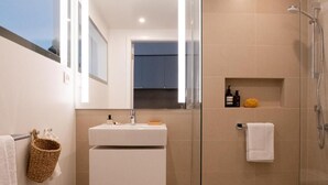 A modern bathroom with a glass-enclosed shower, a white sink with a mirror above it, and a towel rack with a woven basket. - THE FLAG Lugano Self Check-in (Massagno)