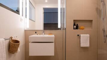 A modern bathroom with a glass-enclosed shower, a white sink with a mirror above it, and a towel rack with a woven basket.