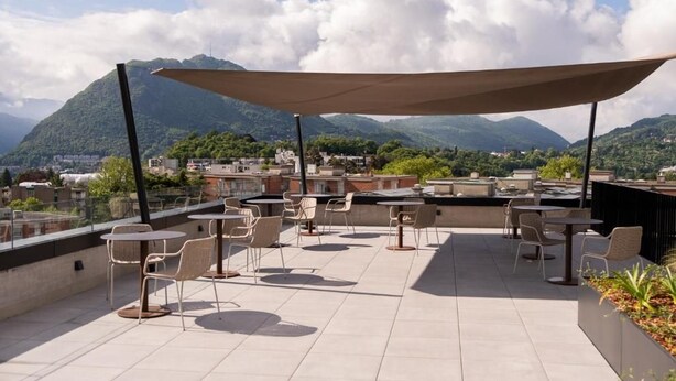 A rooftop terrace with outdoor seating and a view of a mountainous landscape. - THE FLAG Lugano Self Check-in (Massagno)