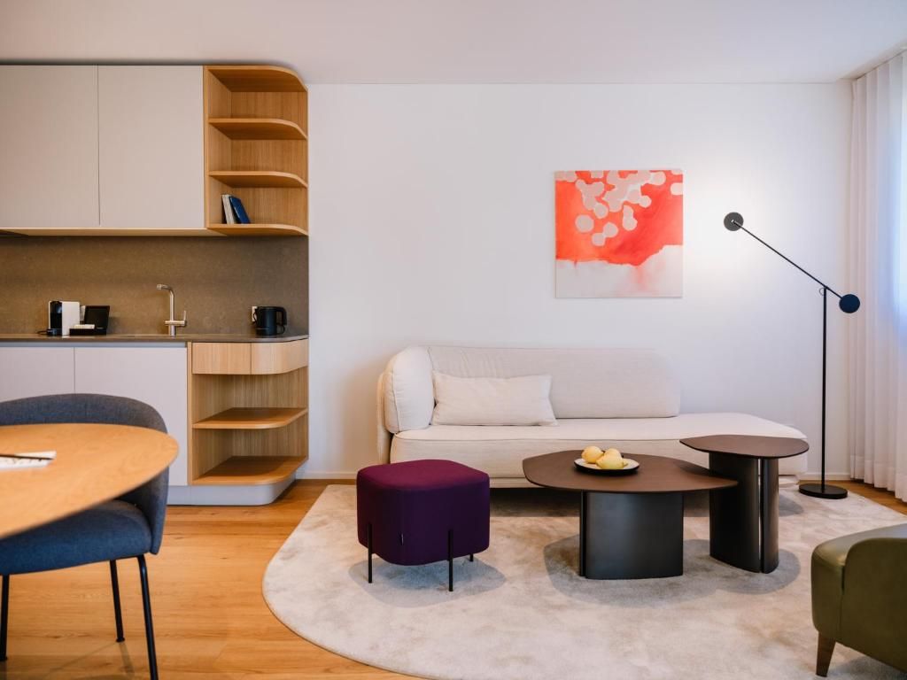 A modern living room with a sofa, coffee table, ottoman, and a dining area with a table and chairs.