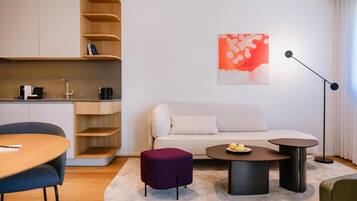 A modern living room with a sofa, coffee table, ottoman, and a dining area with a table and chairs.