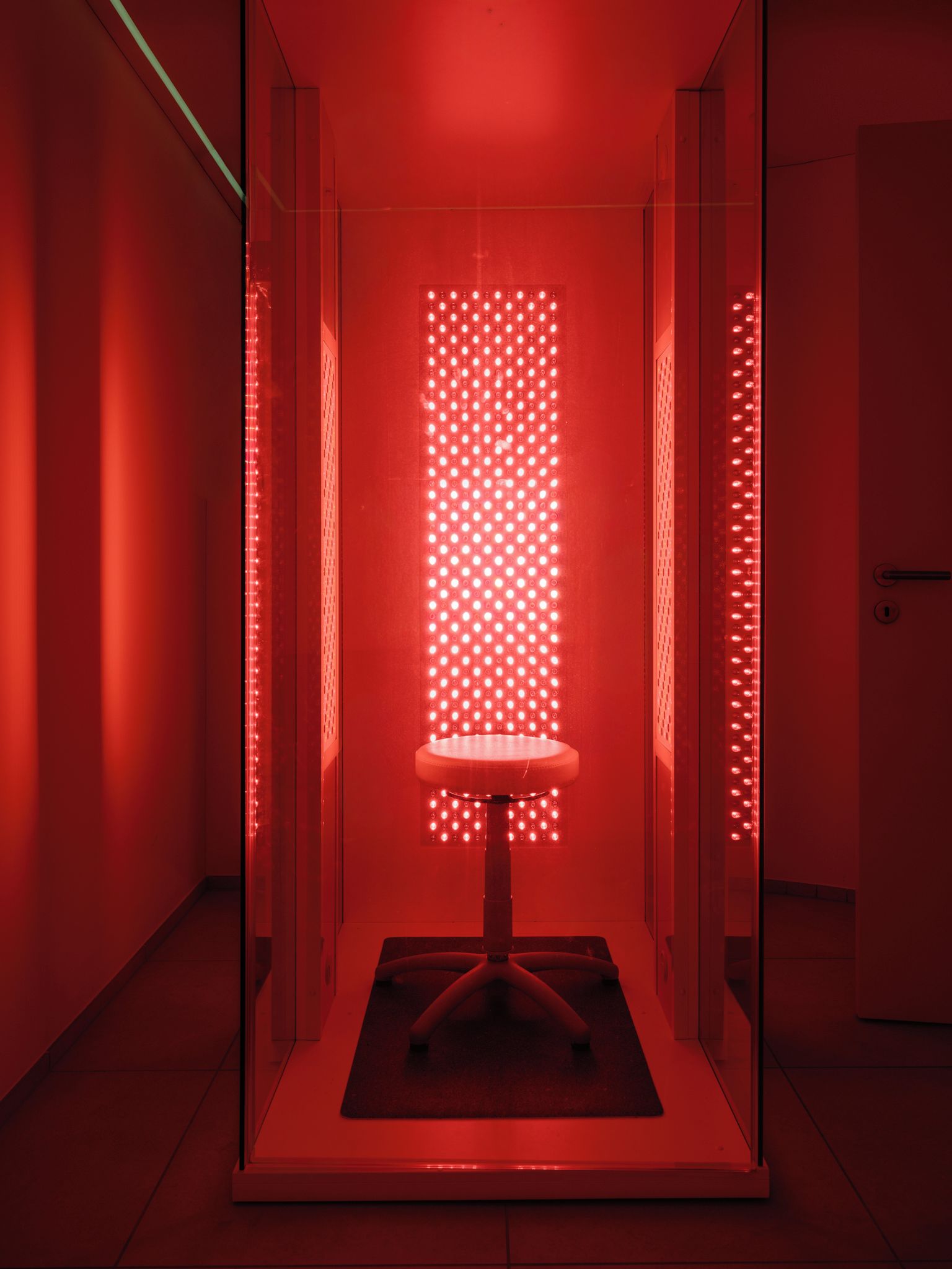 Una stanza con un divisorio in vetro, una sedia e un pannello luminoso rosso.