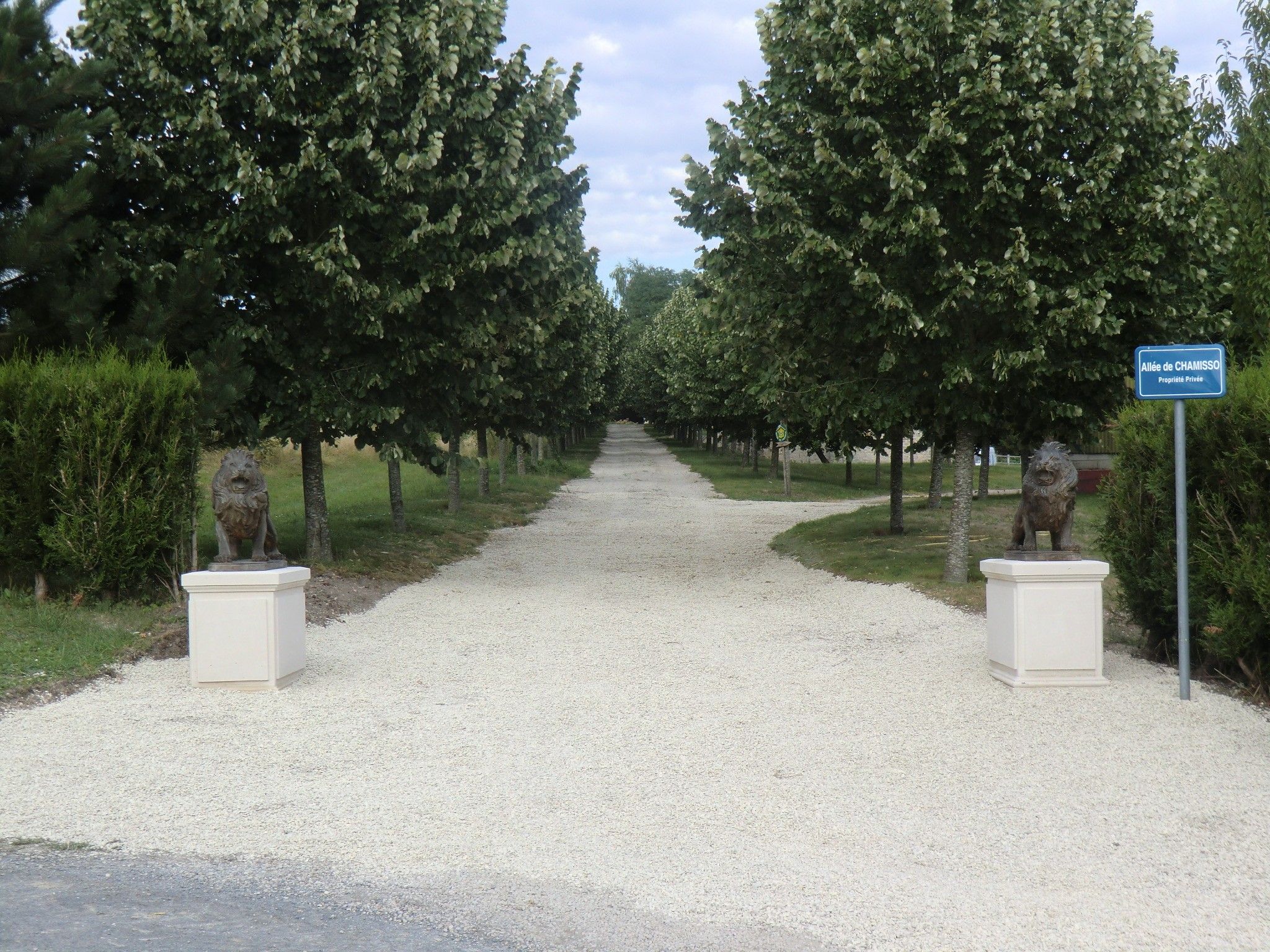 Un chemin de gravier bordé d’arbres et de statues, qui mène à un panneau indiquant qu’il s’agit d’une propriété privée.