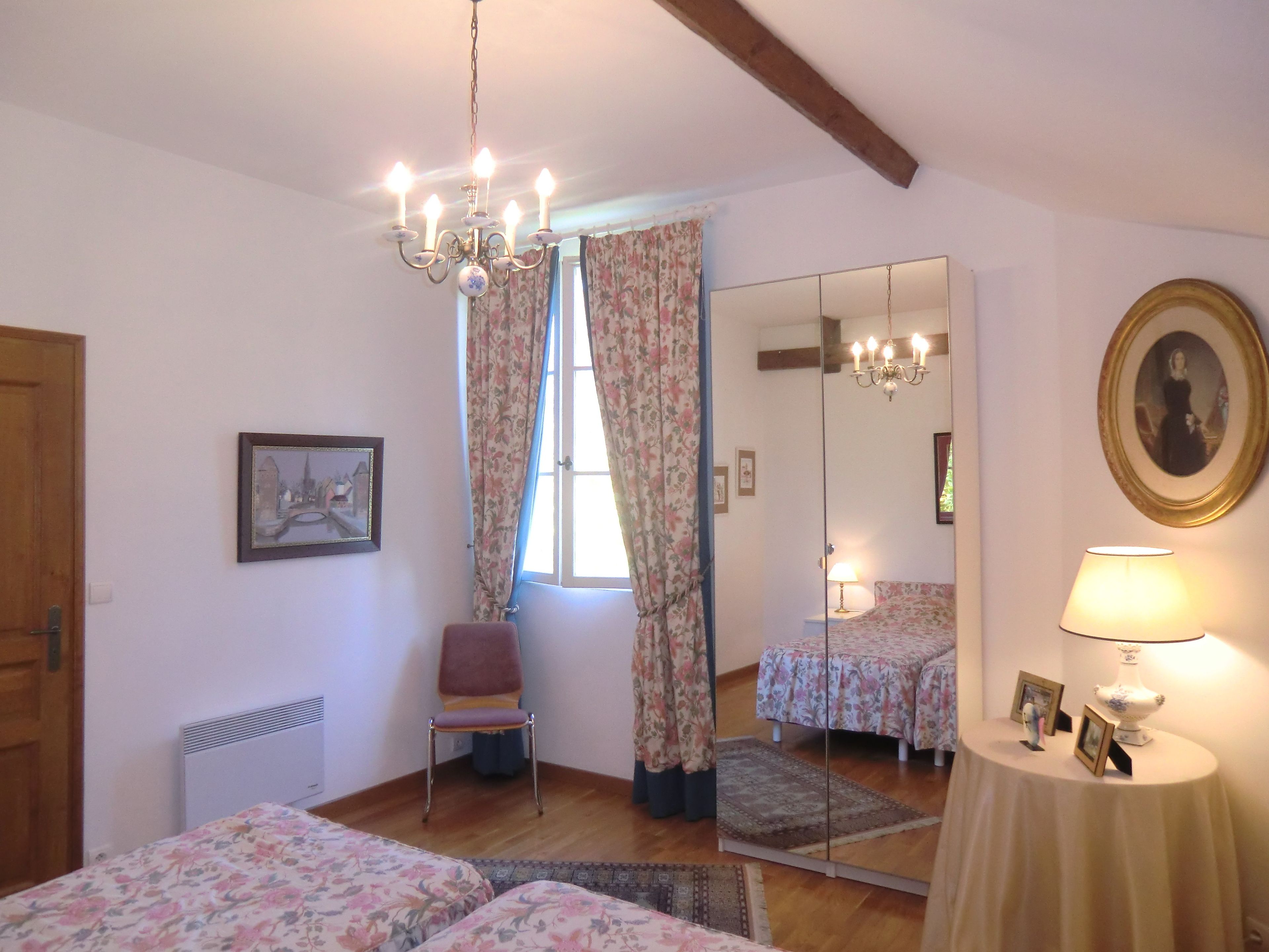 A bedroom with a bed, a chair, a mirror, and a table with a lamp.